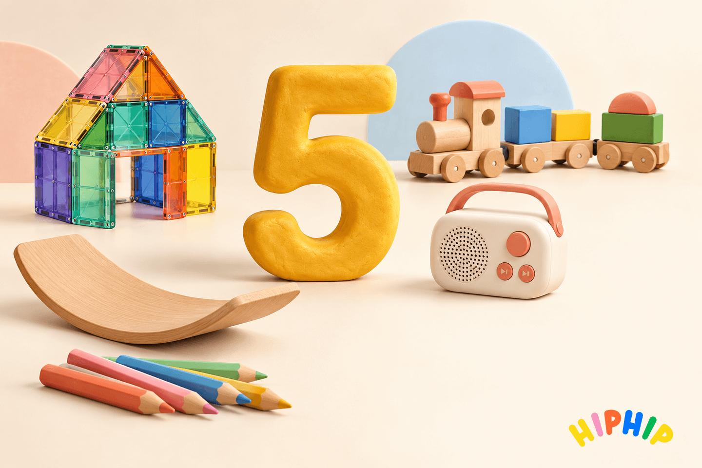 A golden modelling-clay number five surrounded by colourful magnetic tiles, a wooden train, an audio player, a balance board and art pencils, with the hip hip logo.